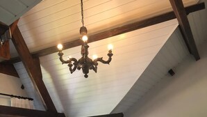 Un dormitorio con techo inclinado, vigas de madera a la vista, una araña, una cama con una manta verde, una mesita de noche con lámpara y un cuadro enmarcado en la pared.