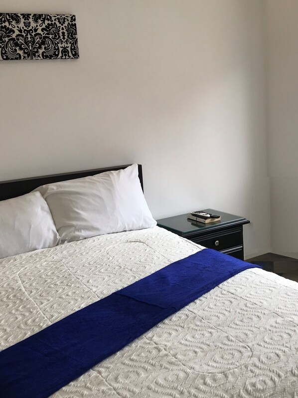 A neatly made bed with white and blue bedding, a black headboard, and a small bedside table with a remote control. - Walkable to Downtown/Stadium/Hosp. St Ines. 360 View of Cuenca - Condo + Terrace (Cuenca)
