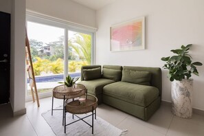 Una sala de estar con un sofá verde, dos sillones de mimbre, una planta grande en maceta y un cuadro en la pared.