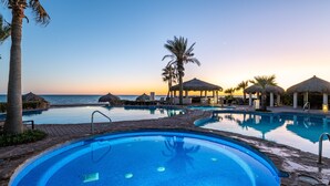 A pool area with multiple pools, palm trees, and thatched-roof structures. - Luna Blanca 1201 by Kivoya (Puerto Peñasco)