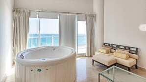 A modern bathroom with a freestanding bathtub, a glass table, and a beige sofa with cushions. - Luna Blanca 1201 by Kivoya (Puerto Peñasco)