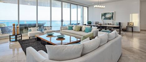A spacious living room with a large window overlooking the ocean, a modern chandelier, and a dining area with a view.