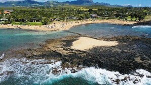 A coastal beach with clear waters, rocky areas, and a backdrop of mountains.