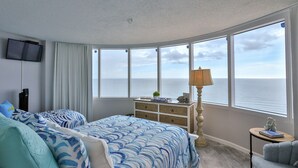 Une chambre avec deux lits, une télévision, une commode, une lampe et une vue sur la mer.
