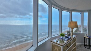 Une pièce dotée de grandes fenêtres donnant sur une plage, d’une lampe et d’une petite table agrémentée d’objets décoratifs.