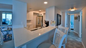 Une cuisine moderne avec des meubles blancs, un réfrigérateur en acier inoxydable et un coin bar doté de chaises blanches.
