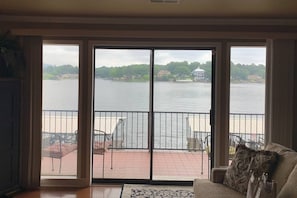 Enjoy a room with a sliding glass door leading to a furnished outdoor deck offering a view of a body of water and distant shoreline.