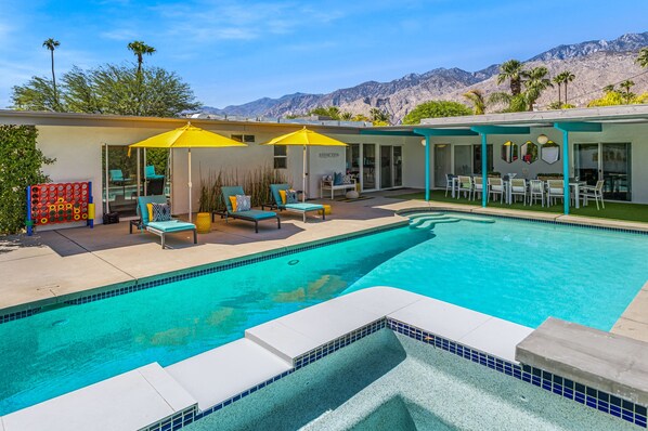 Un espace piscine avec des chaises longues et des parasols, un coin salon abrité et une vue sur les montagnes.