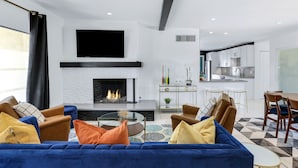 Un salon moderne avec une cheminée, un canapé bleu et un coin repas comprenant une table et des chaises.