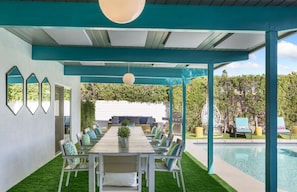 A covered outdoor dining area with a pool in the background.