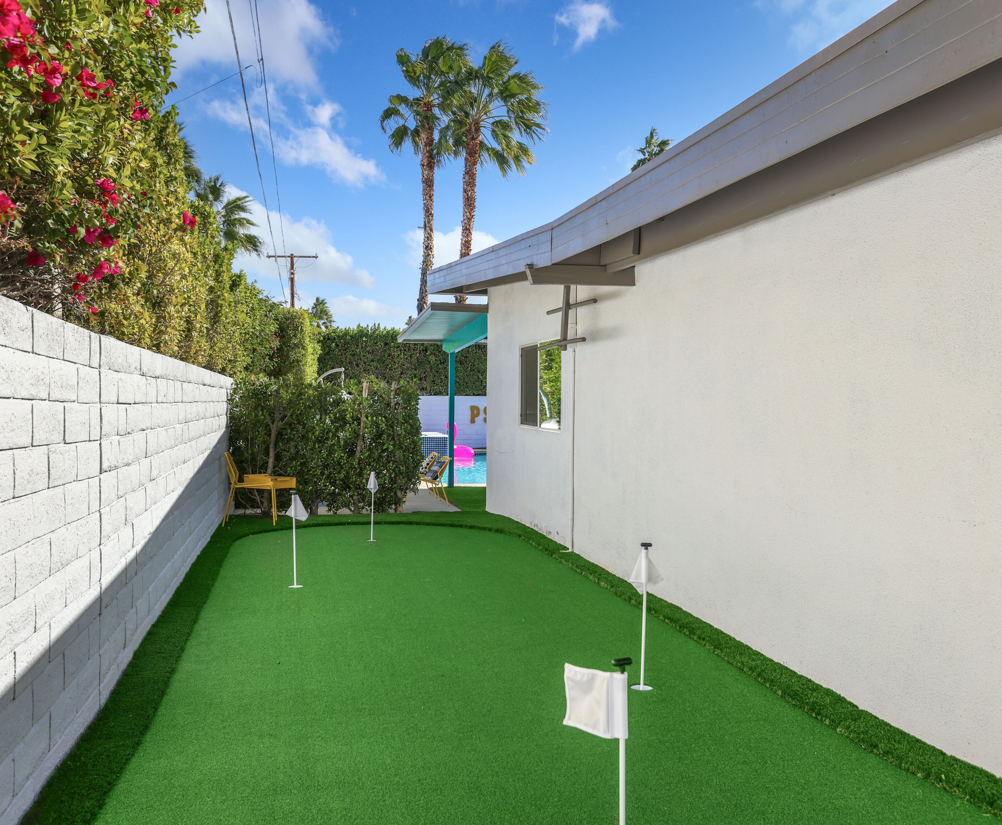 A small, enclosed space with artificial green turf, a white wall, and a brick wall on one side.