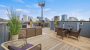 A rooftop terrace with wicker furniture, a table, and a potted plant. - Night Lounge | Luxe Rooftop Retreat + City Views (Nashville)