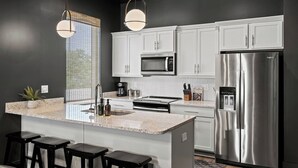 A modern kitchen with white cabinets, a stainless steel refrigerator, a microwave, and a granite countertop. - Night Lounge | Luxe Rooftop Retreat + City Views (Nashville)