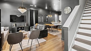 A modern living room with a sofa, dining table, and chairs, a kitchen area, and a staircase. - Night Lounge | Luxe Rooftop Retreat + City Views (Nashville)