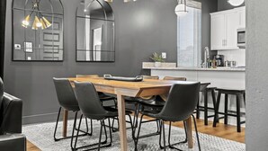 A modern dining area with a wooden table and black chairs, a kitchen with white cabinets, and pendant lighting. - Night Lounge | Luxe Rooftop Retreat + City Views (Nashville)