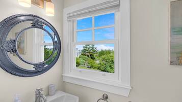 A bathroom with a large ornate mirror, a white sink, a window with a view of greenery, and a towel rack.