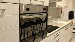 Een moderne keuken met witte kasten, een inbouwoven, een fornuis en een bar met krukken.