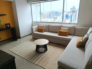 Un salon moderne avec un canapé, une table basse et une vue sur le paysage urbain, grâce à de grandes fenêtres.