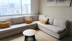 A modern living room with a sectional sofa, a round coffee table, and a large window offering a city view.