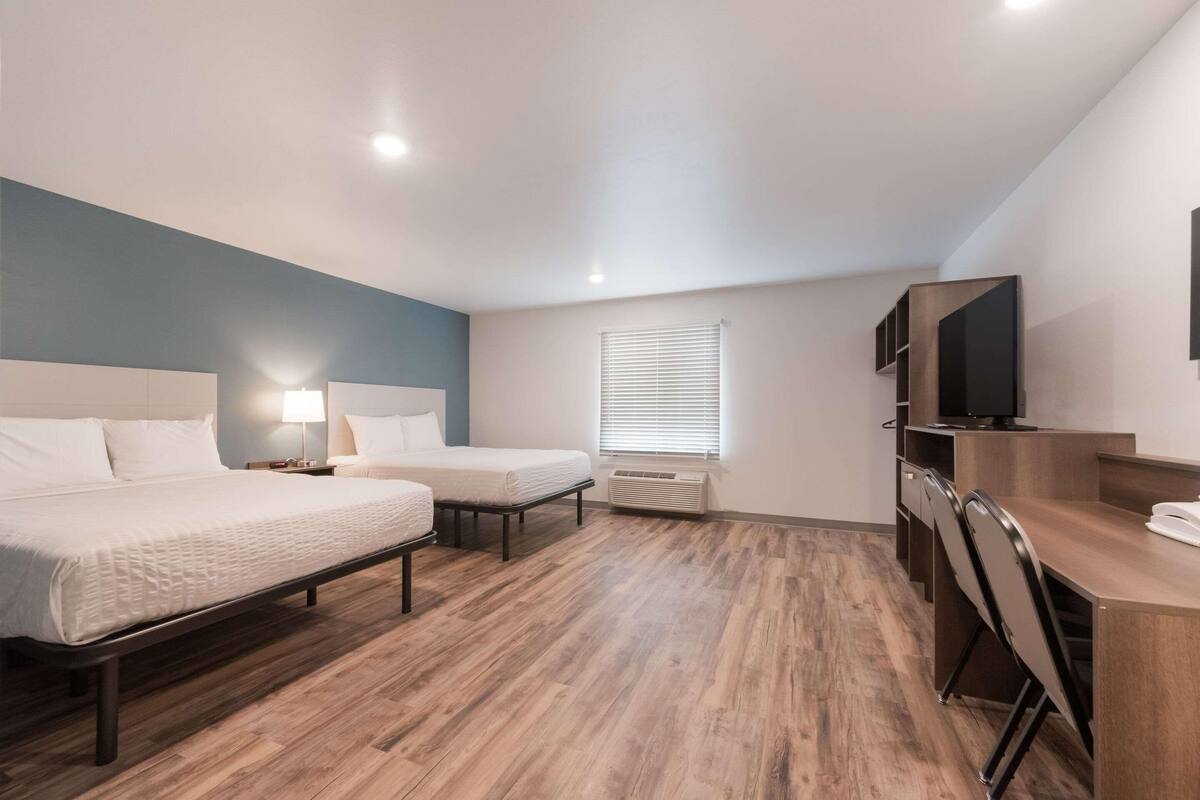 A hotel room with two beds, a desk, a TV, and a window with blinds.