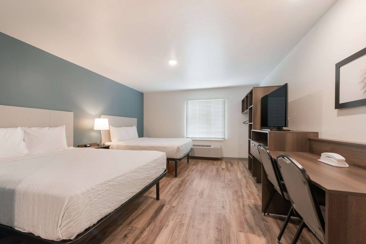 A hotel room with two beds, a desk with a chair, a television, and a window with blinds.