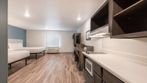 A compact kitchenette with a built-in stove, a sink, and a microwave. There are two beds with white bedding and a window with blinds. - Woodspring Suites Philadelphia Northeast (Philadelphia)
