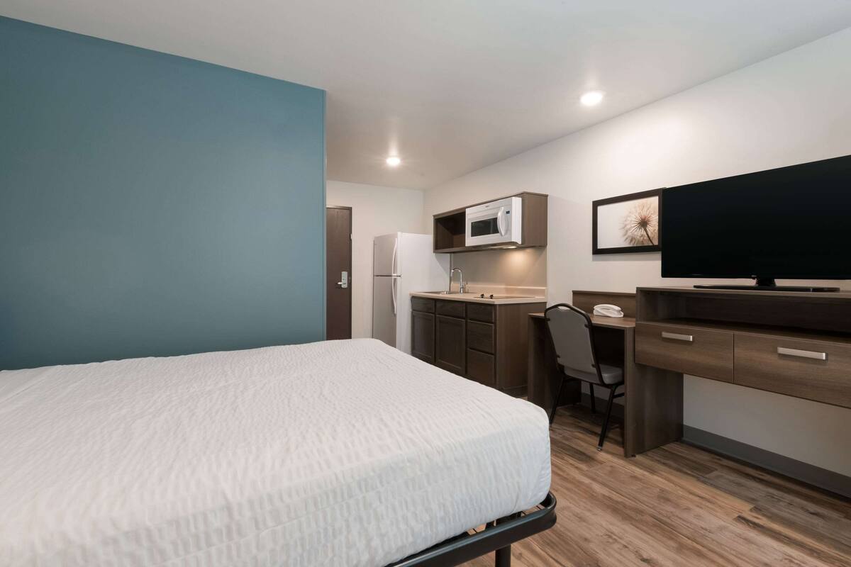 A compact room with a bed, kitchenette, and a desk with a chair.