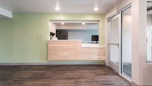 A reception area with a wooden reception desk, a computer, and a glass door leading to another room. - Woodspring Suites Philadelphia Northeast (Philadelphia)