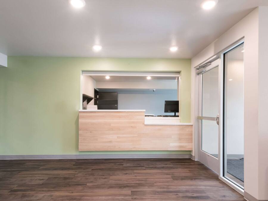 A reception area with a wooden reception desk, a computer, and a glass door leading to another room.