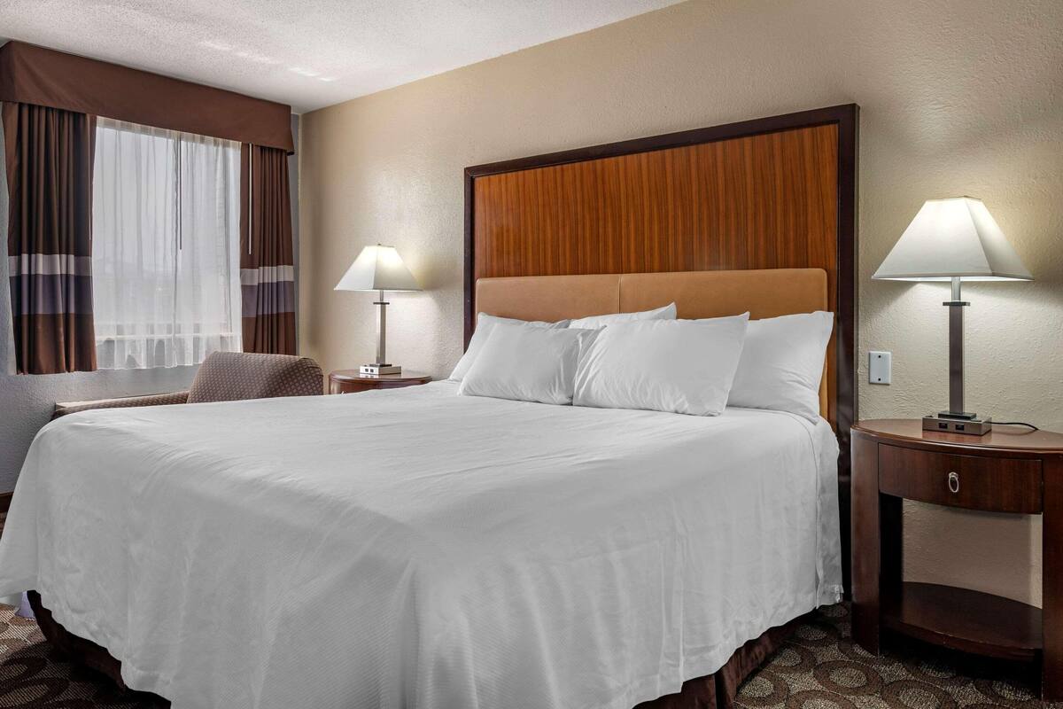 A hotel room with a large bed, two bedside tables, a chair, and a window with curtains.