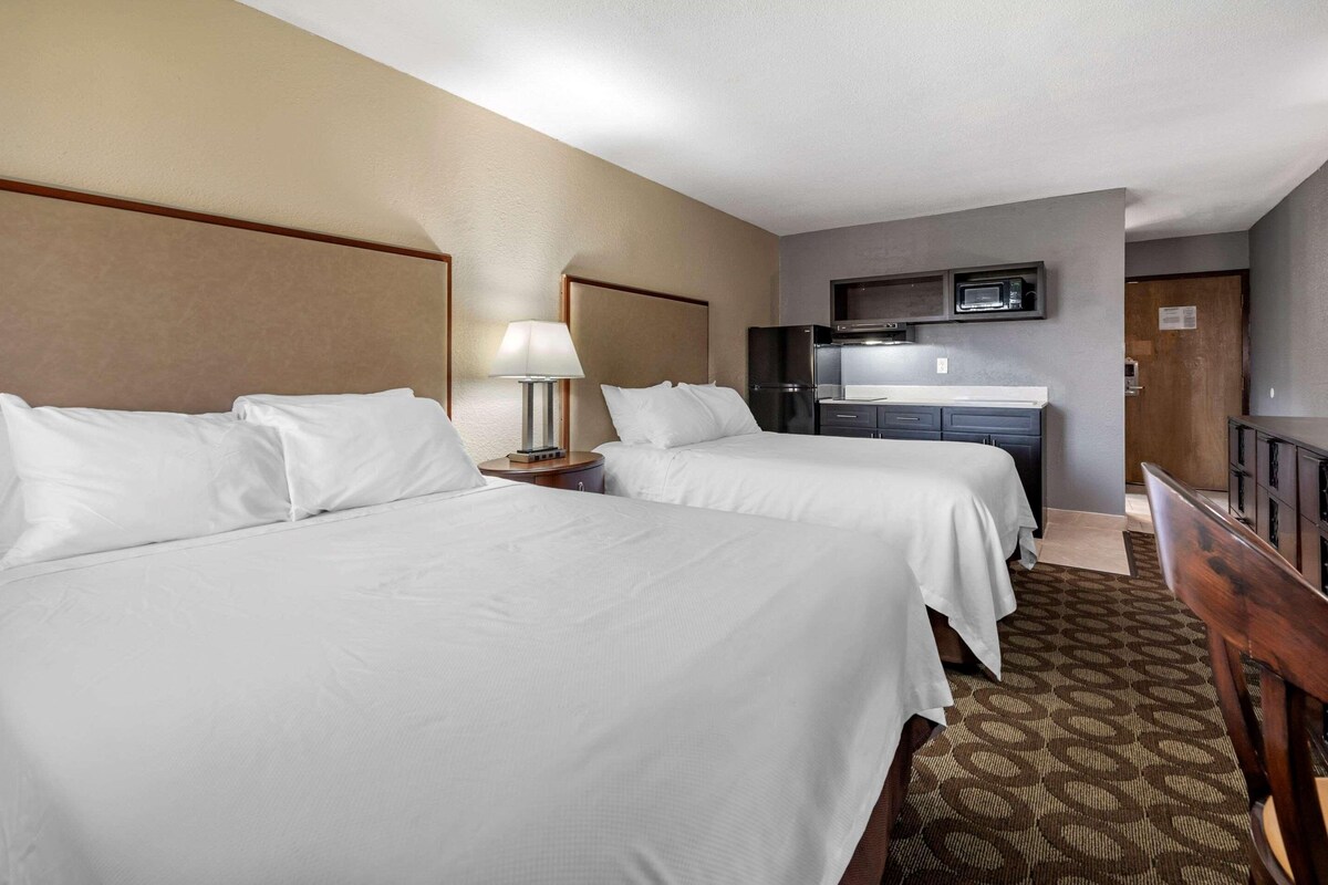 A hotel room with two beds, a desk, a microwave, and a TV.