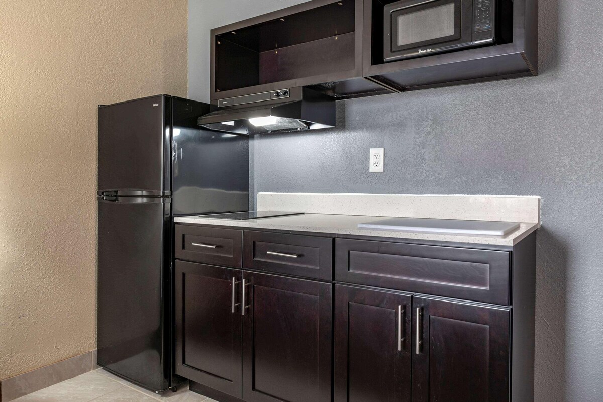 A compact kitchen with a built-in microwave, a stainless steel range hood, and dark wooden cabinets.