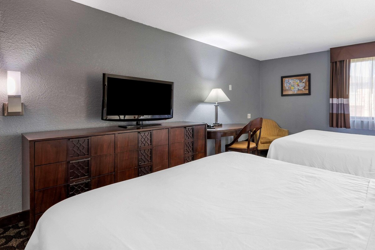 Ein Hotelzimmer mit zwei Betten, einem Fernseher, einem Schreibtisch mit Lampe und einem Sessel.