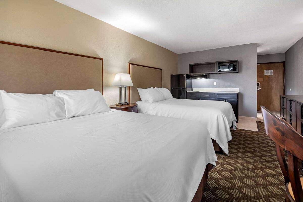 A hotel room with two beds, a desk, a microwave, and a TV.