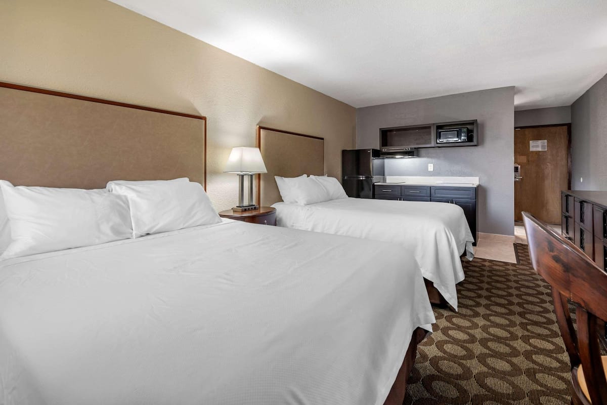 A hotel room with two beds, a desk, a microwave, and a TV.