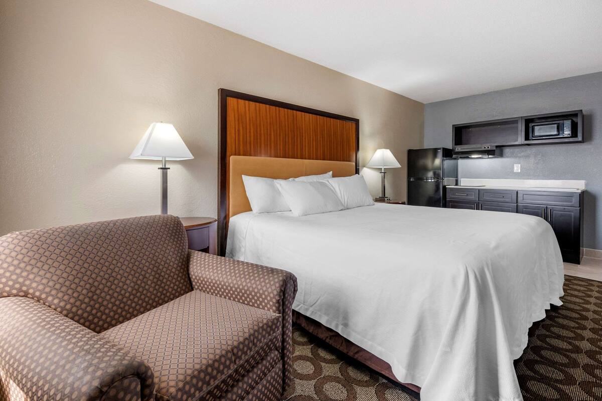 A hotel room with a bed, a chair, a desk, and a kitchenette.
