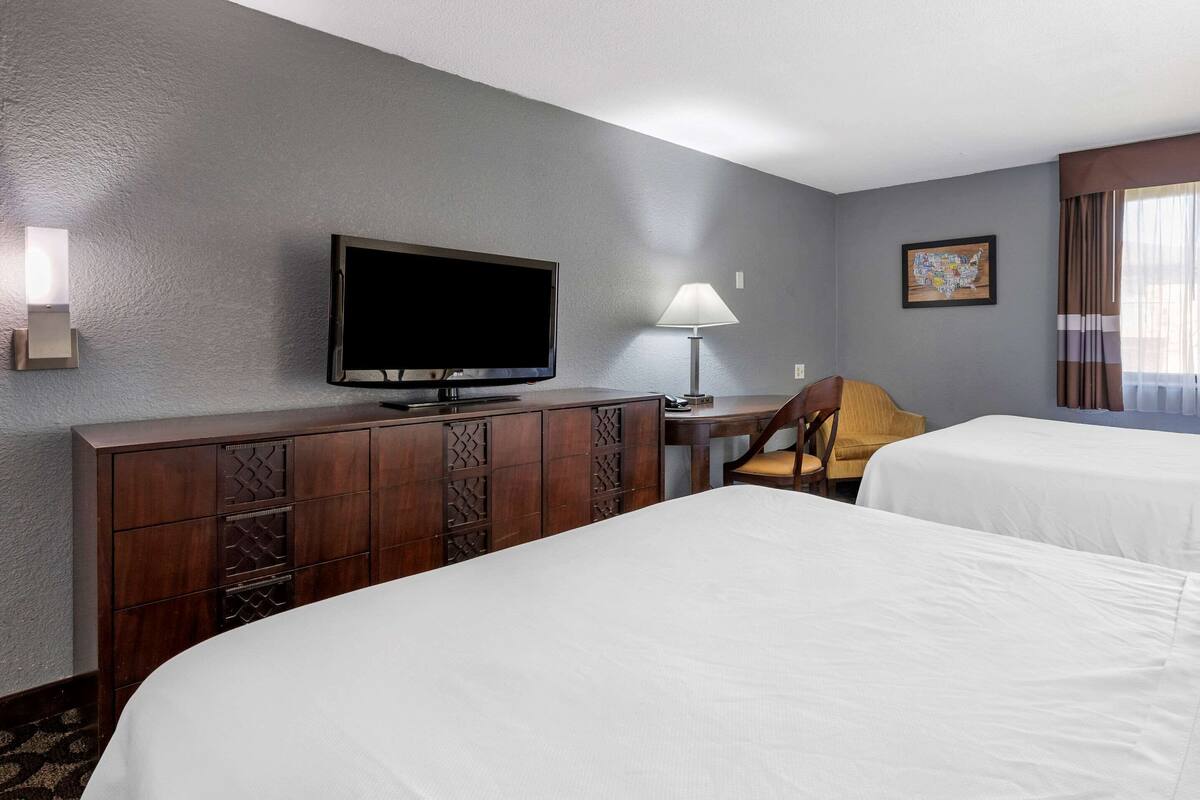 A hotel room with two beds, a TV, a desk with a lamp, and a map on the wall.