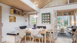 Une pièce chaleureuse avec un plafond en bois, une table à manger avec des chaises, un canapé et une grande fenêtre donnant sur un paysage verdoyant.