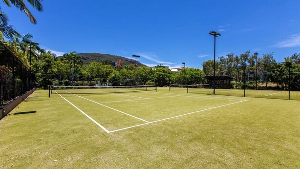 Un court de tennis avec un filet, entouré d’arbres et sous un ciel dégagé.