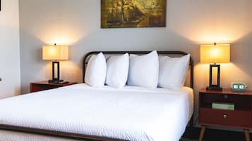 Una cama bien tendida con sábanas blancas, dos mesitas de noche con lámparas, un reloj de pared y un cuadro sobre la cama.
