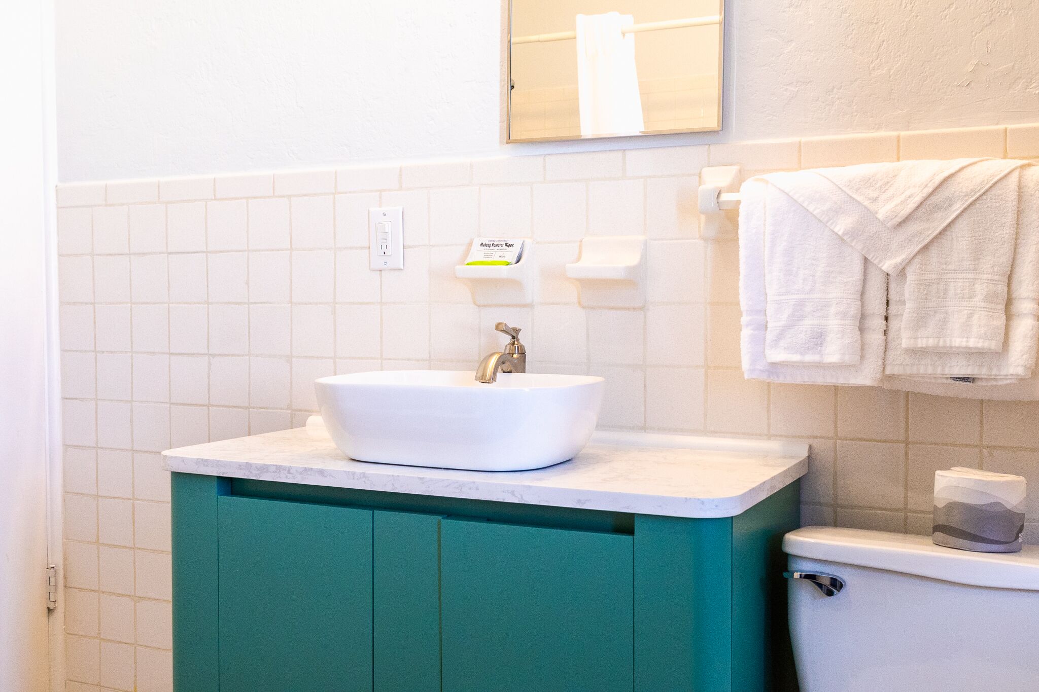 Une salle de bain avec un lavabo blanc, des meubles turquoise et des toilettes.