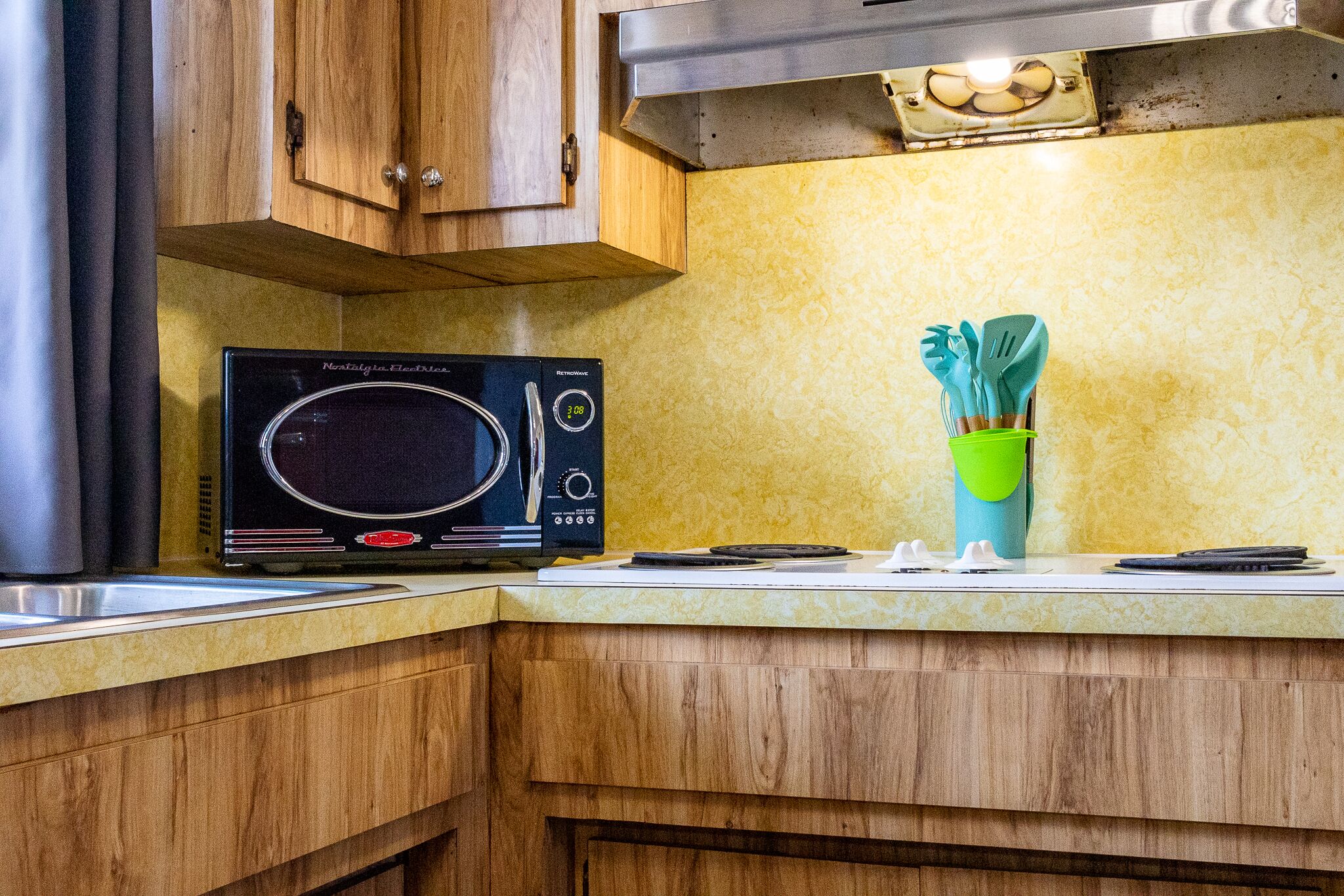 Una cocina con armarios de madera, microondas y un portalapices verde.