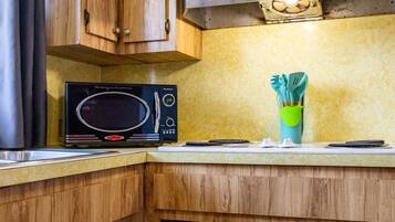 Een keuken met houten kastjes, een magnetron en een groene houder voor bestek.