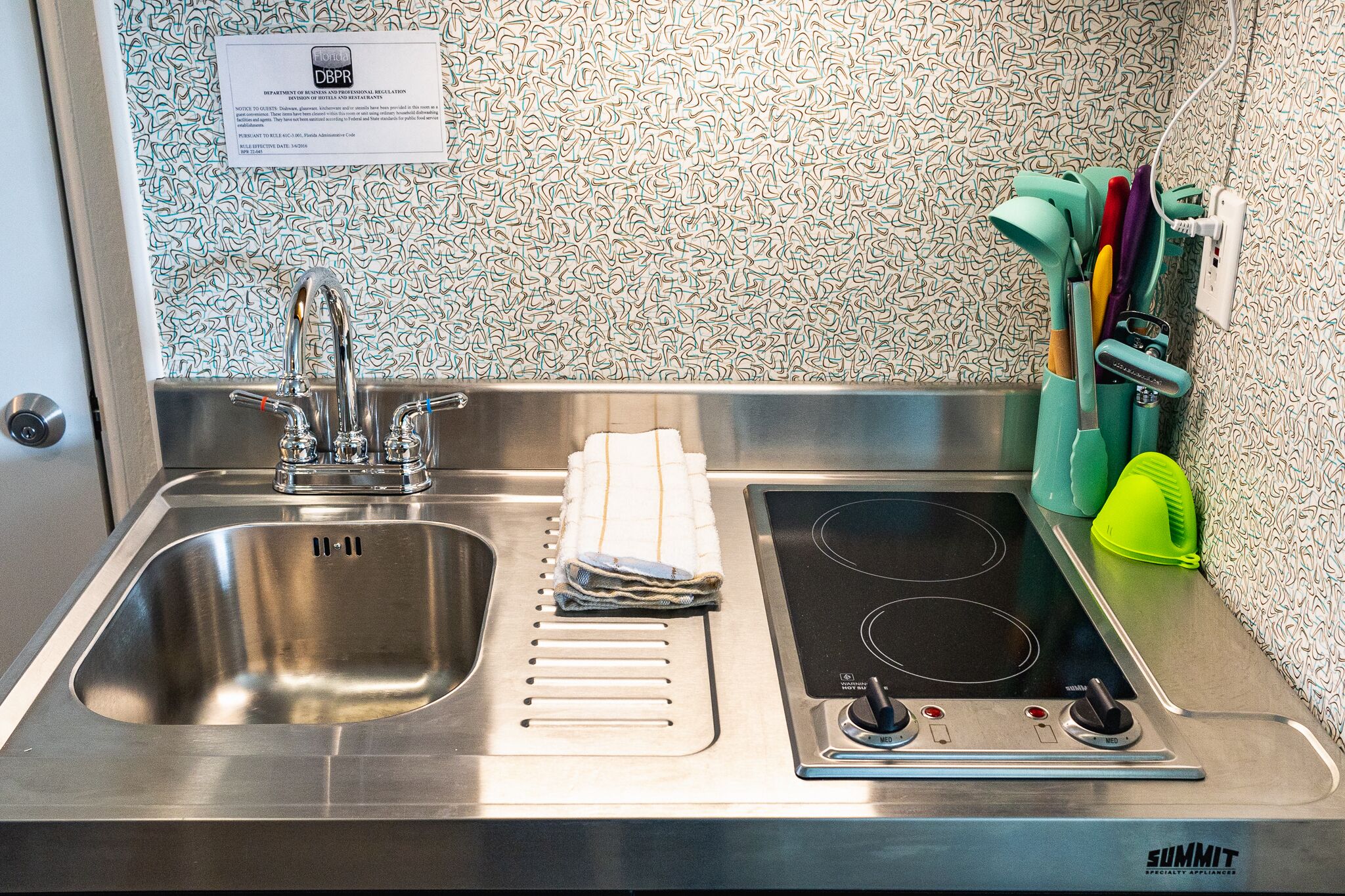 A stainless steel sink with a faucet, a dish drying rack, and a built-in electric stovetop.