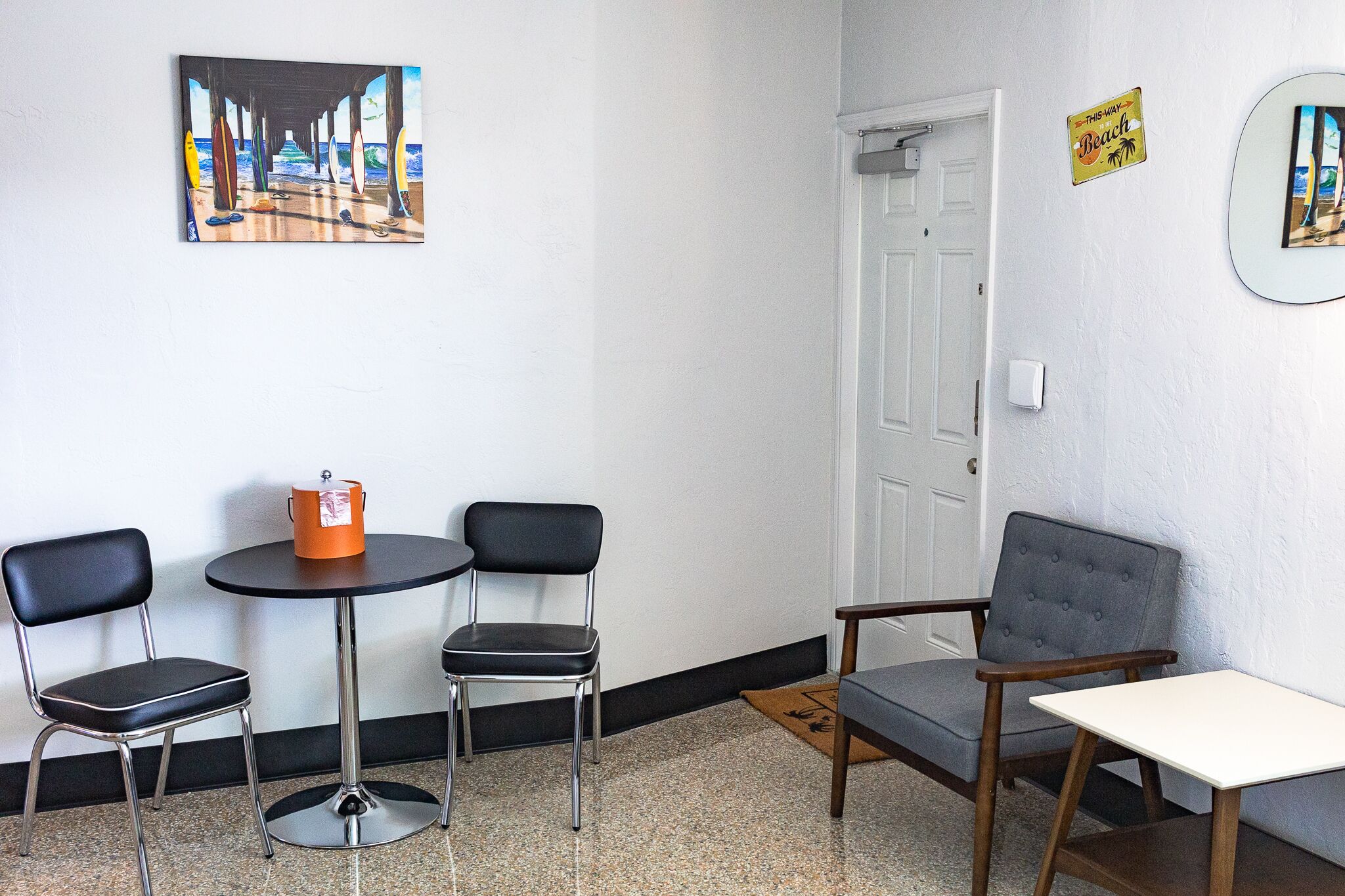 Una habitación con una mesa redonda, dos sillas, un pequeño cubo naranja y una puerta.