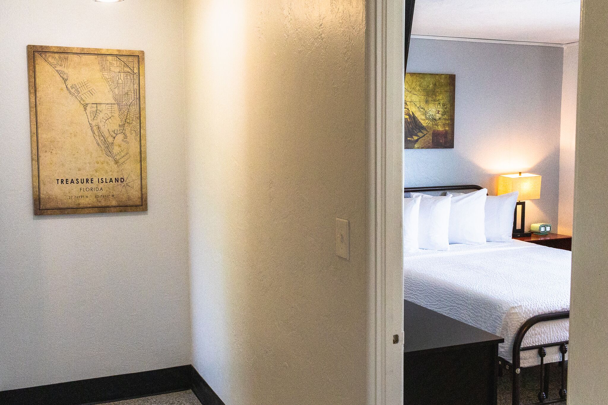 A hotel room with a bed, a nightstand with a lamp, and a map on the wall.