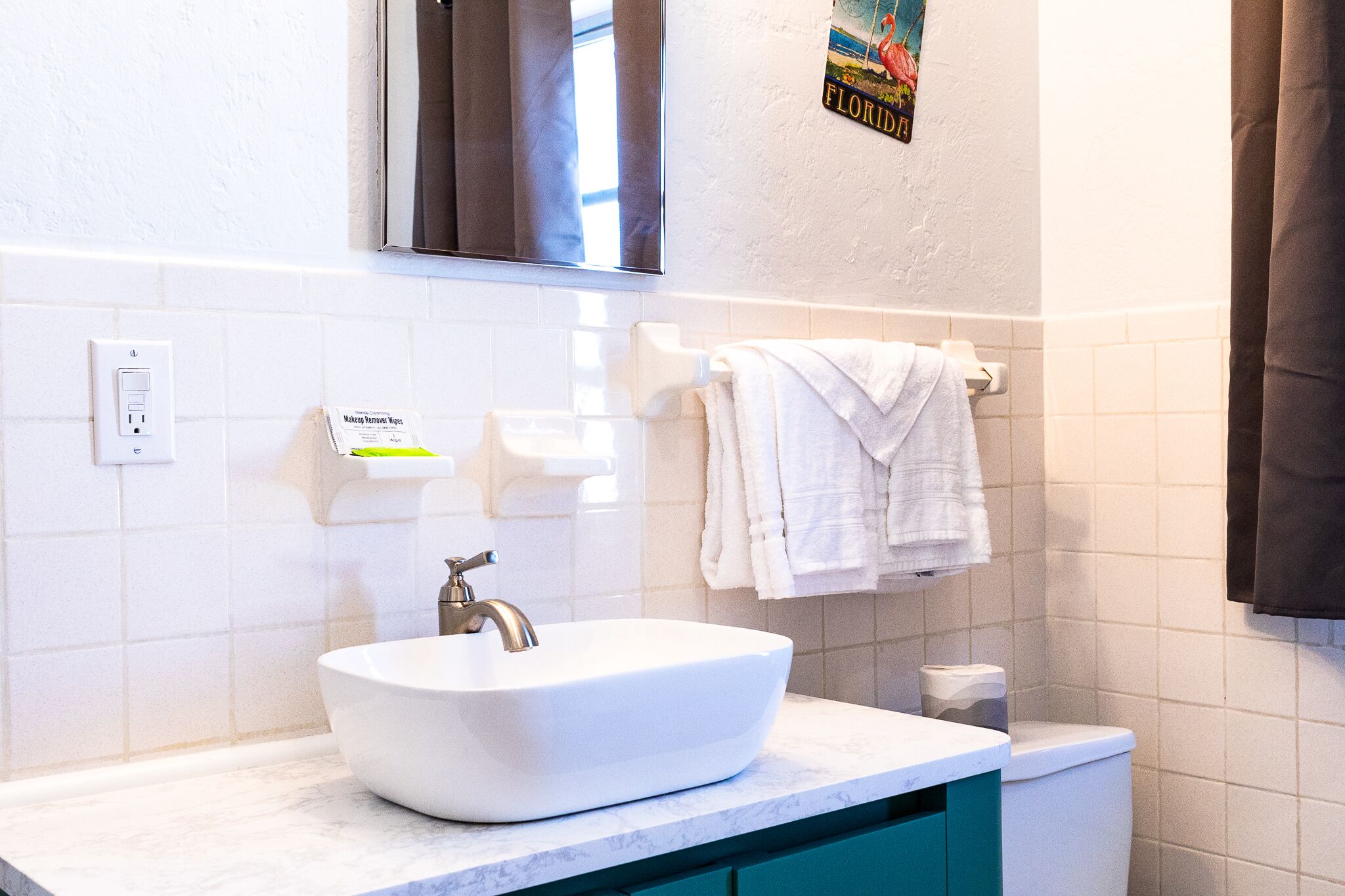 Un baño con lavamanos blanco, espejo, toallero y retrete.