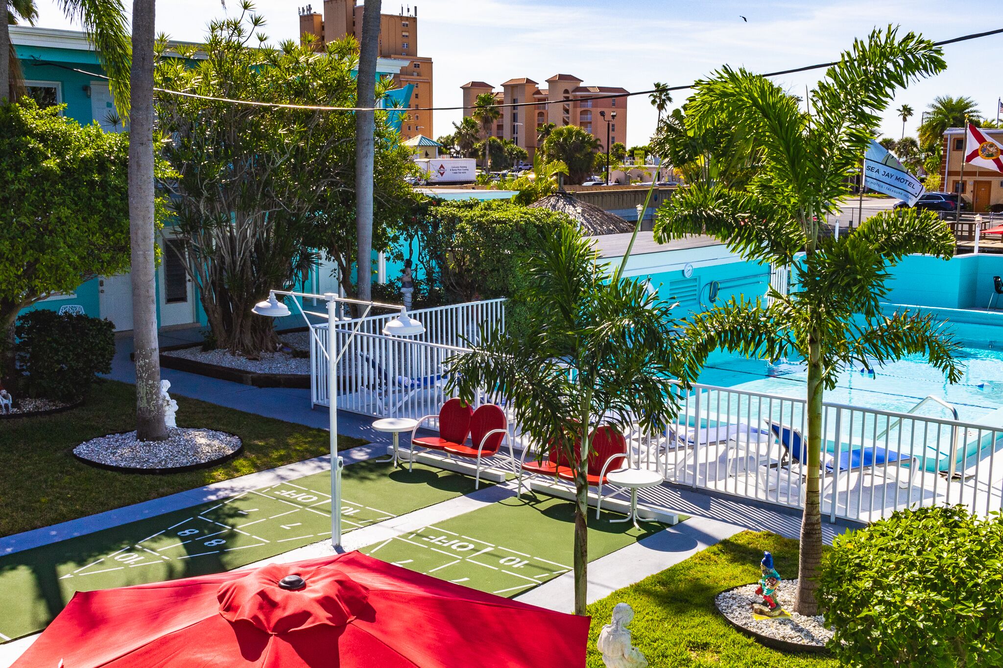 Un área de piscina con canchas de juego de bolos, sillas de descanso y un paraguas rojo.