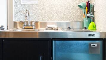 Una cocina compacta con un refrigerador de acero inoxidable, un mueble de madera sobre el lavamanos y un salpicadero con diseño.