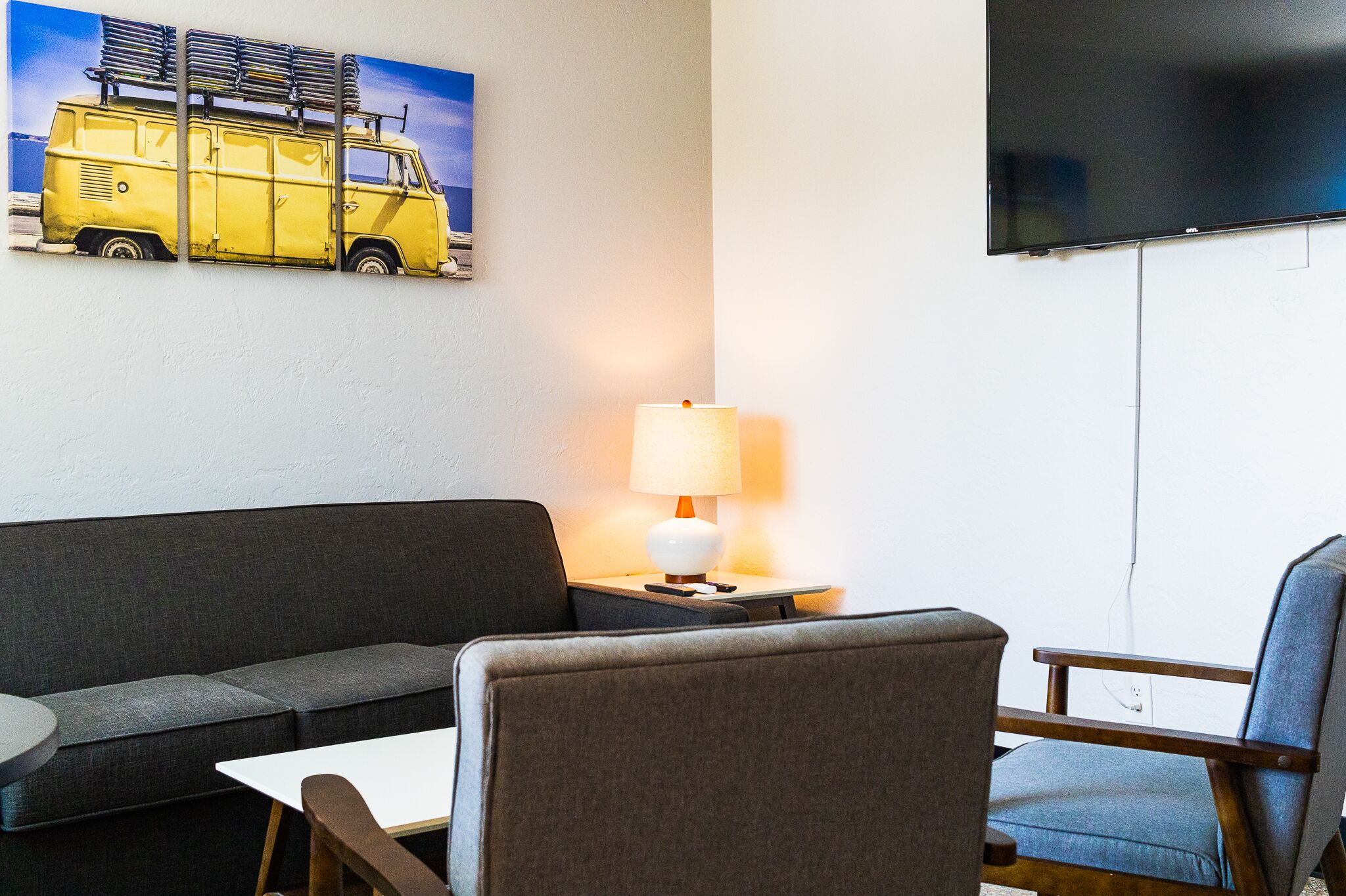 Una habitación con un sofá gris, una mesita, una lámpara y un televisor montado en la pared.
